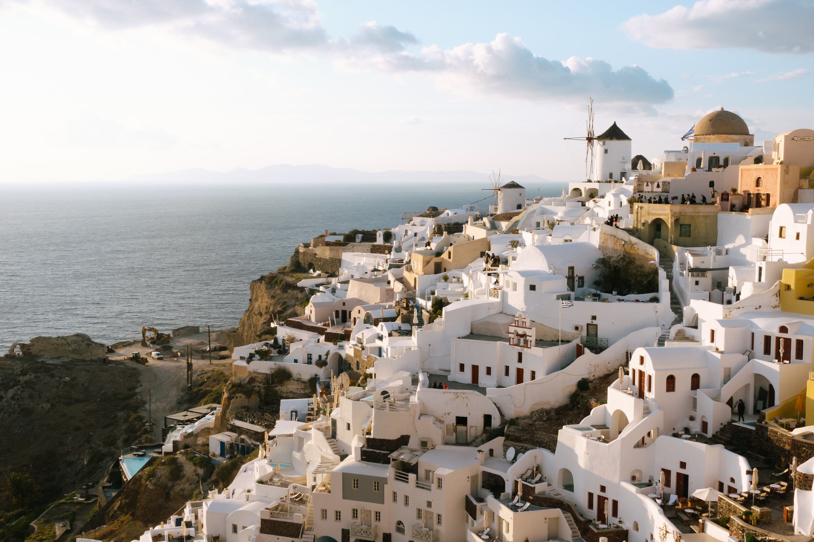 White-washed buildings and windmills cascading down a cliff overlooking the Aegean Sea in Oia, Santorini, Greece